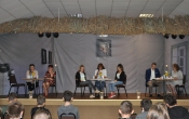 Siedmioro lektorów siedzi na scenie przy stolikach