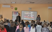 Mężczyzna i kobieta stoją twarza do siedzących na ławkach dzieci.